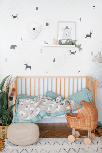 The cot is spread out. We see a crumpled pillow, plaid and blanket. The toy is also in bed. There is a toy baby stroller nearby.