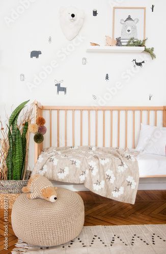 The cot is spread out. We see a crumpled pillow, plaid and blanket. The toy is also in bed. There is a toy baby stroller nearby. photo