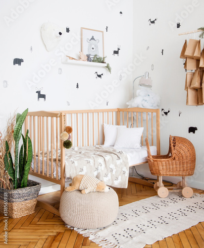 The cot is spread out. We see a crumpled pillow, plaid and blanket. The toy is also in bed. There is a toy baby stroller nearby.