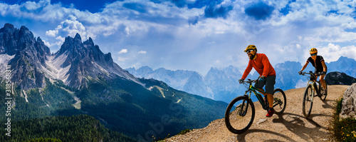 Fototapeta Naklejka Na Ścianę i Meble -  Cycling woman and man riding on bikes in Dolomites mountains andscape. Couple cycling MTB enduro trail track. Outdoor sport activity.