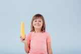smiling girl has a corn in her hand. isolated on blue background, copy space, in studio, profile view