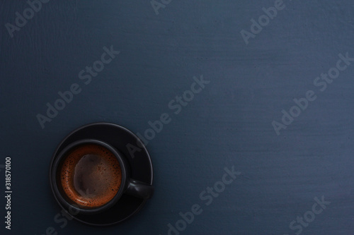 Dark grey cup of coffee on blue table. Hot drink concept. Coffee shop, espresso, top view, copy space