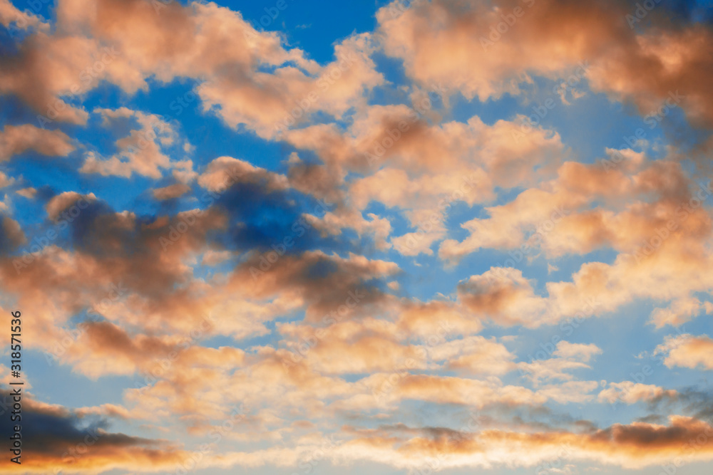 Beautiful yellow-orange dramatic cumulus clouds in the blue sky at sunset
