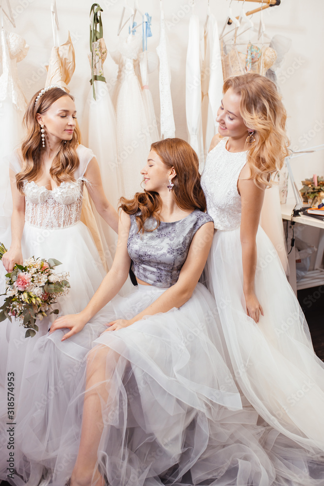 portrait of three beautiful brides or fiancee posing at camera together, wearing white wedding dresses, attractive romantic girls in wedding salon portrait of three beautiful brides or fiancee posing at camera together, wearing white wedding dresses, attractive romantic girls in wedding salon