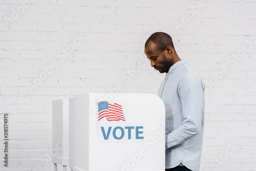 african american citizen voting near stand with vote lettering photo