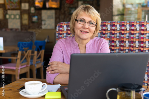 A woman with a laptop looks at a document in a cafe, office