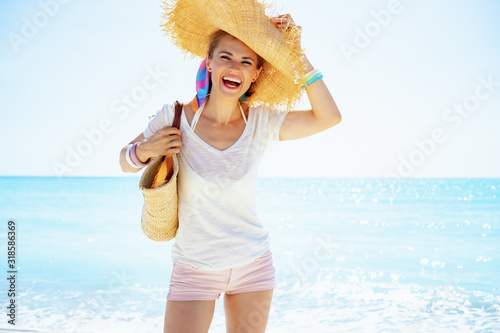 happy young woman with beach straw bag and big hat on seashore
