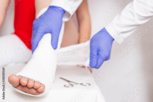 Doctor traumatologist establishes a fixing bandage to a girl athlete on the ankle joint. The concept of dislocation and sprain on the leg of athletes, hospital