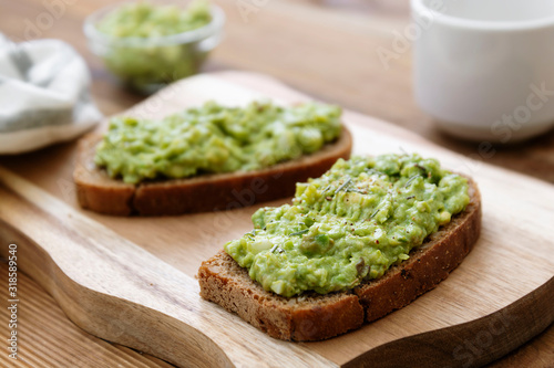 Healthy food. Rye bread with guakomole, avocado pasta on wooden cutting board. Avocado toast for breakfast.