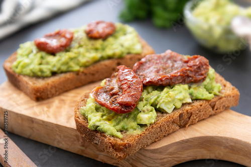 Vegetarian food. Rye bread with guakomole, avocado pasta and dried tomatoes, on wooden cutting board. Avocado toast.