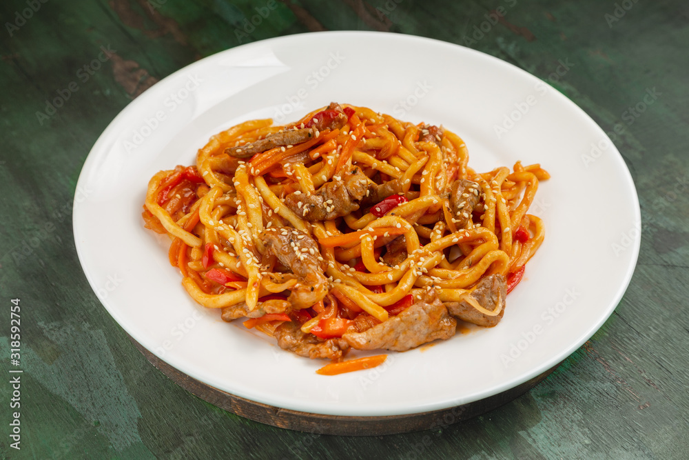 Wok noodles with meat and vegetables in a white plate on a wooden background Wok noodles with meat and vegetables in a white plate on a wooden background