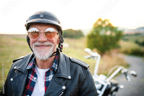 Fotografia A cheerful senior man traveller with motorbike in countryside, headshot