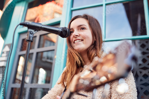 Female Musician Busking Playing Acoustic Guitar And Singing Outdoors In Street photo