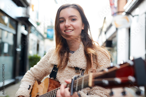 Portrait Of Young Female Musician Busking Playing Acoustic Guitar And Singing Outdoors In Street photo