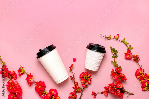 Coffee or tea paper cup  spring branches of red flowers on pink background top view flat lay copy space. Take away coffee cup  mockup. Spring coffee concept  layout for design. Spring flowering