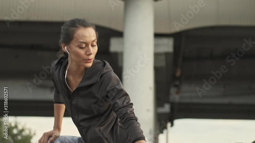 Side view of Calm pretty asian sports woman in earphones warming up and looking away outdoors photo