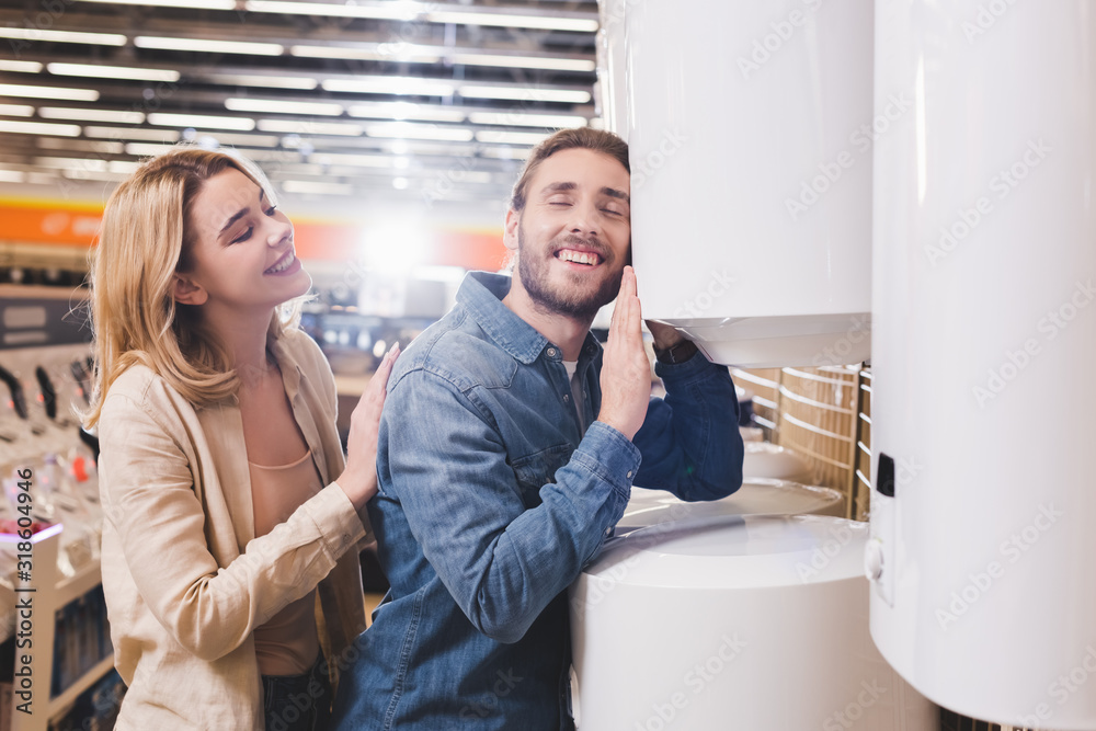 smiling boyfriend touching boiler and girlfriend looking at him in home appliance store smiling boyfriend touching boiler and girlfriend looking at him in home appliance store