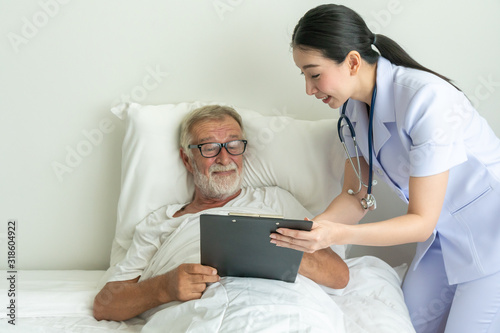Female nurse showing health check report in chart board to senior man on patient bed - Image