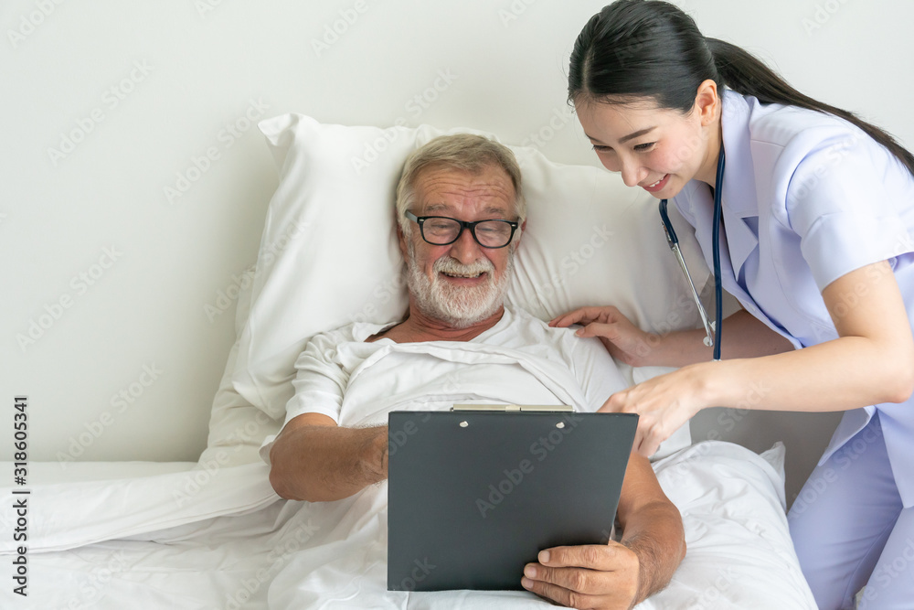 Female nurse showing health check report in chart board to senior man on patient bed - Image Female nurse showing health check report in chart board to senior man on patient bed - Image