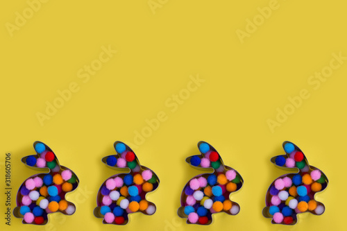 Four abbit bunny shaped forms with colorful balls inside on yellow background. Easter concept. Flat lay with place for text.