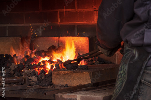 The blacksmith holds the workpiece with a tick in the flame of the furnace