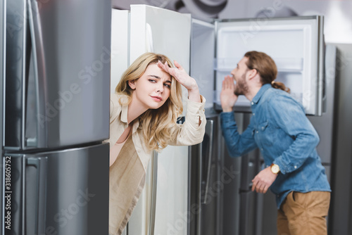 selective focus of curious girlfriend and boyfriend looking at fridge on background in home appliance store
