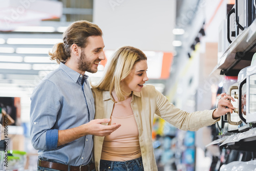 smiling consultant and woman looking at microwave in home appliance store