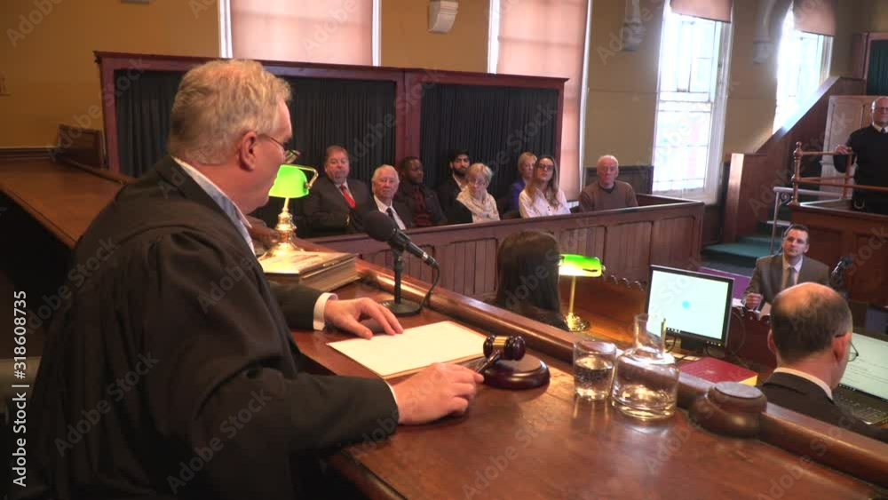 Male Judge hitting the gavel in a Court. The magistrate is calling order in the courtroom / courthouse with Jury behind