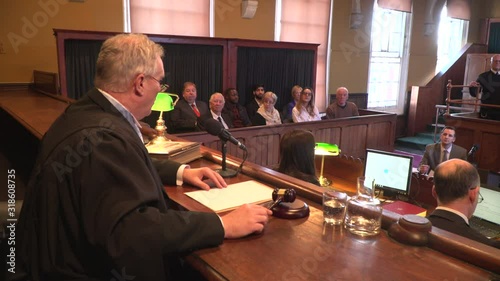 Male Judge hitting the gavel in a Court. The magistrate is calling order in the courtroom / courthouse with Jury behind