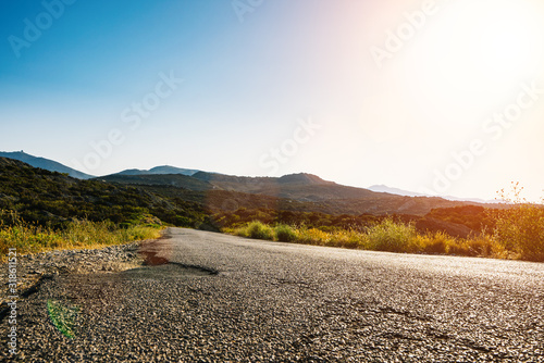 Fototapeta Empty long mountain road to the horizon on a sunny summer day at bright sunset