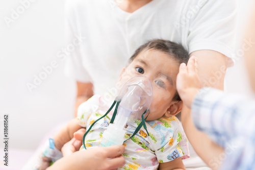 Asian little baby boy is is treated respiratory problem with vapor nebulizer and sister's hand is touching his head to make him feel better, concept of pediatric patient care for sick in the hospital. photo