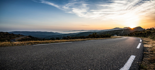 Empty long mountain road to the horizon on a sunny summer day at bright sunset