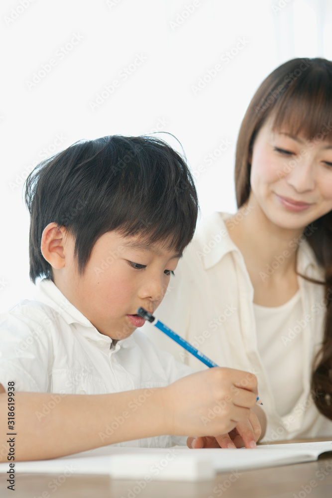 Woman assisting boy writing in notebook Woman assisting boy writing in notebook