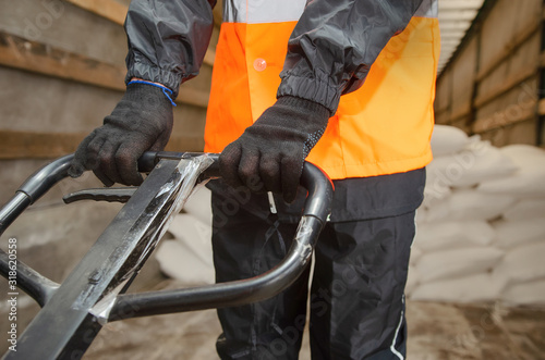  warehouse worker in workwear and safety helmet is working with hand pallet truck or pallet jack and shipments in distribution warehouse