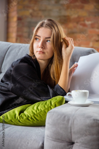 Beauty Day for yourself. Woman wearing silk robe doing her daily skincare routine at home. Lying on sofa, reading magazin, drinking coffee. Concept of beauty, self-care, cosmetics, youth. Close up.