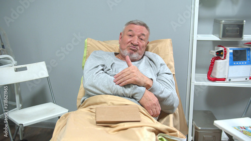 Man lie on bed in the hospital and look at camera with smile