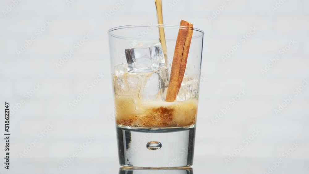 Non-alcoholic refreshing cocktail made of cola, ice, cinnamon. jet of cola pours into rotating glass filled with ice cubes and cinnamon stick. Non-alcoholic refreshing cocktail made of cola, ice, cinnamon. jet of cola pours into rotating glass filled with ice cubes and cinnamon stick.
