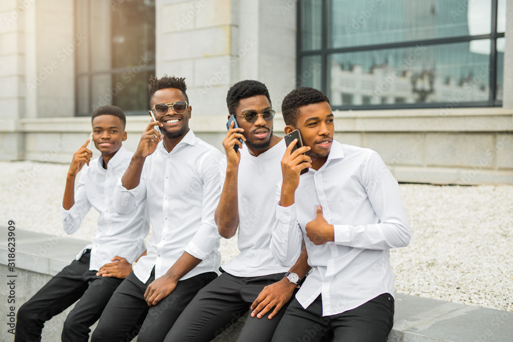 four handsome young african men in white shirts with phones in their hands four handsome young african men in white shirts with phones in their hands