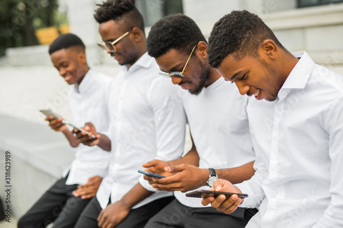 four handsome young african men in white shirts with phones in their hands