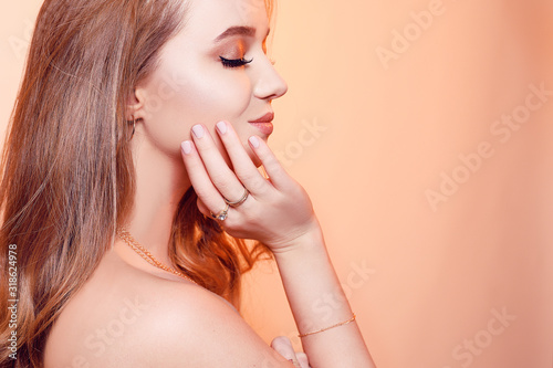 Gorgeous girl with brown hair, a girl with rings, gold, jewelry, necklaces, earrings. The girl touches her face with a hand. Professional makeup is gentle.