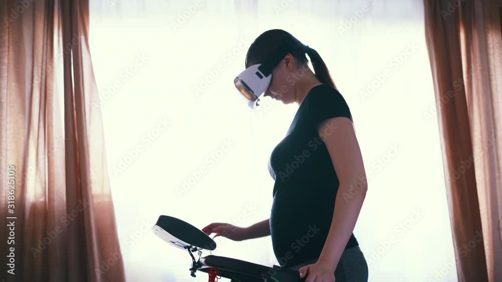 slim woman with virtual reality headset has training on modern treadmill near open window in light room slim woman with virtual reality headset has training on modern treadmill near open window in light room