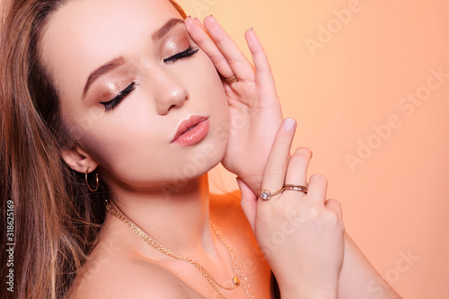 Gorgeous girl with brown hair  a girl with rings  gold  jewelry  necklaces  earrings. The girl touches her face with a hand. Professional makeup is gentle.