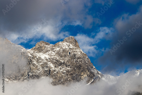 Bergspitze mit etwas Schnee zwischen grauen Wolken