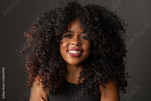 Young afro-american woman with curly hair looking at camera and smiling. Cute afro girl with curly hair smiling looking at camera.