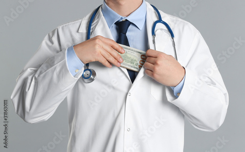 Doctor putting bribe into pocket on grey background, closeup. Corruption in medicine