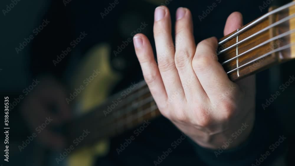 CU: professional musician in black pullover plays simple melody on bass guitar sitting at home close view CU: professional musician in black pullover plays simple melody on bass guitar sitting at home close view
