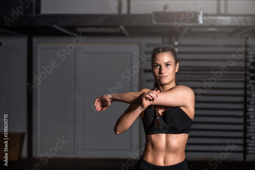 Young beautiful muscular attractive fit girl stretch her hand and body muscles after heavy hardcore cross workout training in the gym close up