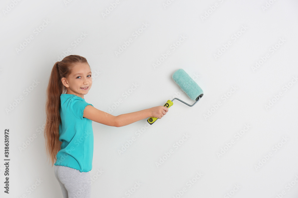 Little child painting with roller brush on white wall indoors Little child painting with roller brush on white wall indoors