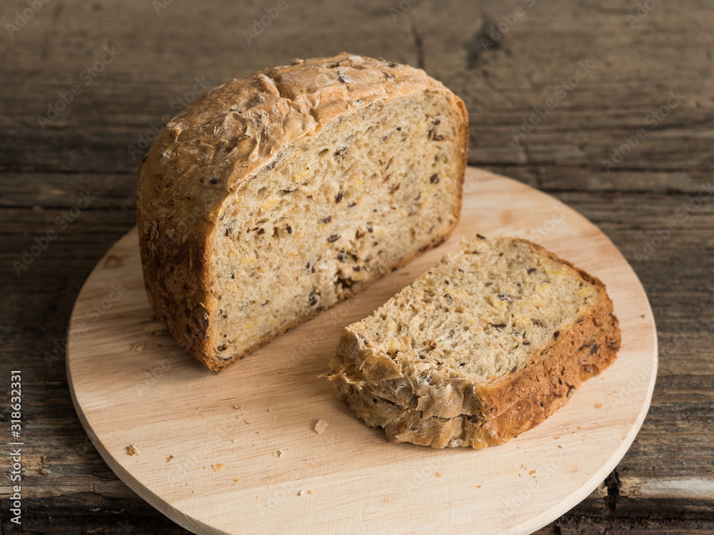 Half a loaf of homemade whole grain bread with various seeds and two slices on a wooden background. Healthy natural fresh food. Close-up