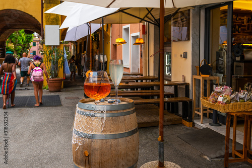 Italian aperitif "aperol stpritz" with ice and a slice of orange in large round glasses on a wooden vintage barrel in a steet bar in Manarola, Italy. © eskstock